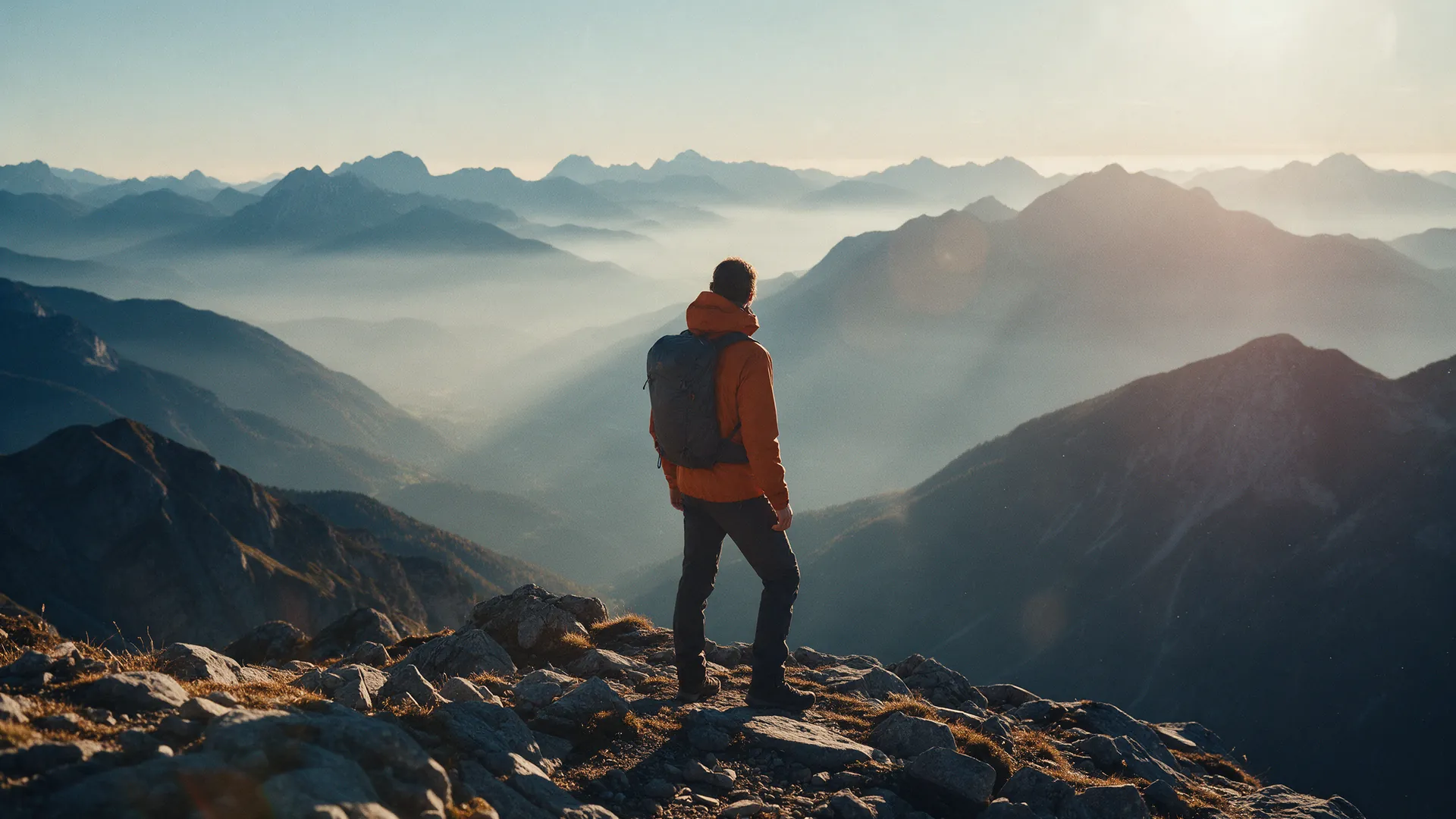 A hiker in an ember shell walking a snow ridge at first light