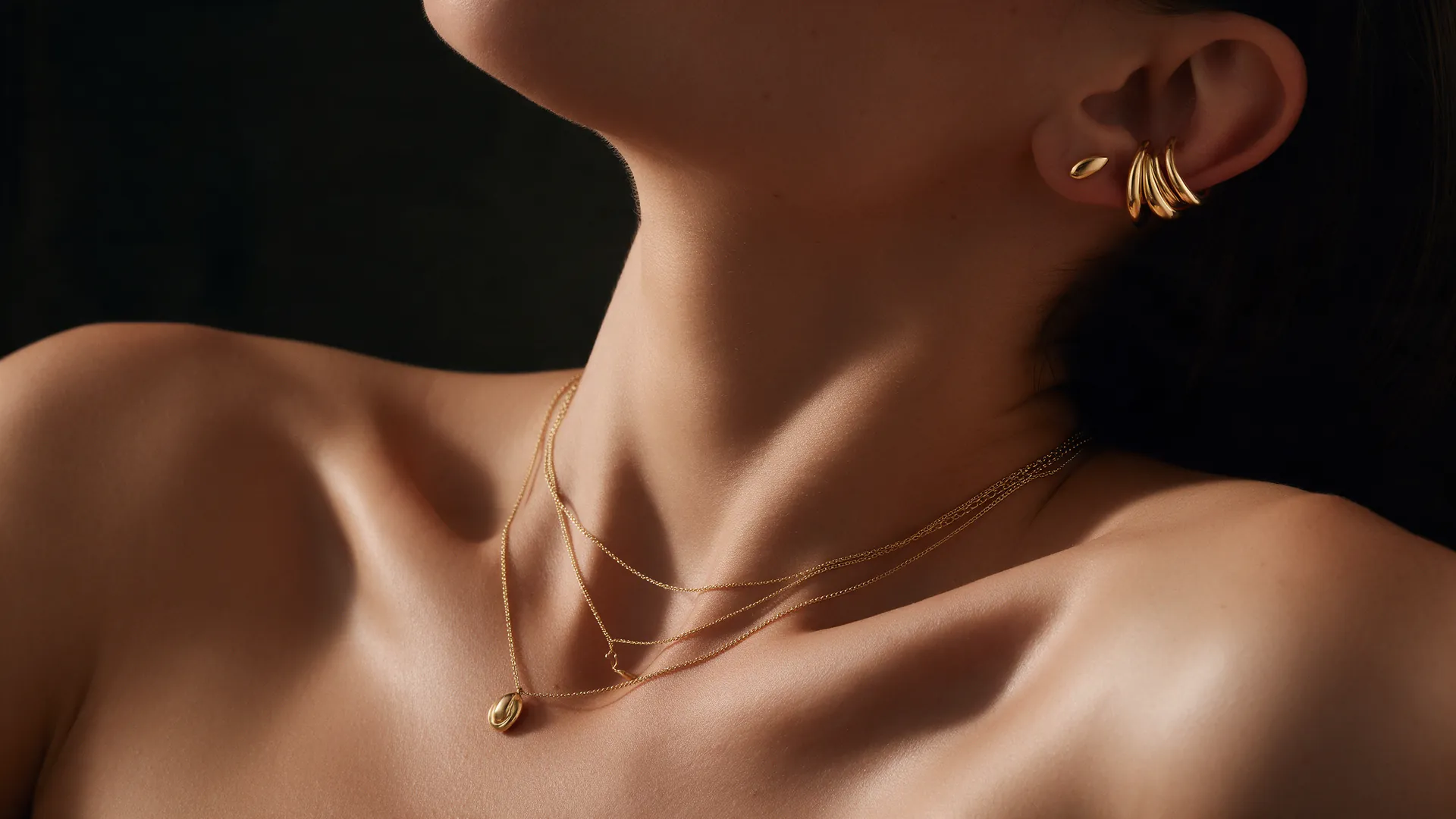 Layered 18k gold chains and ear cuffs worn at the collarbone